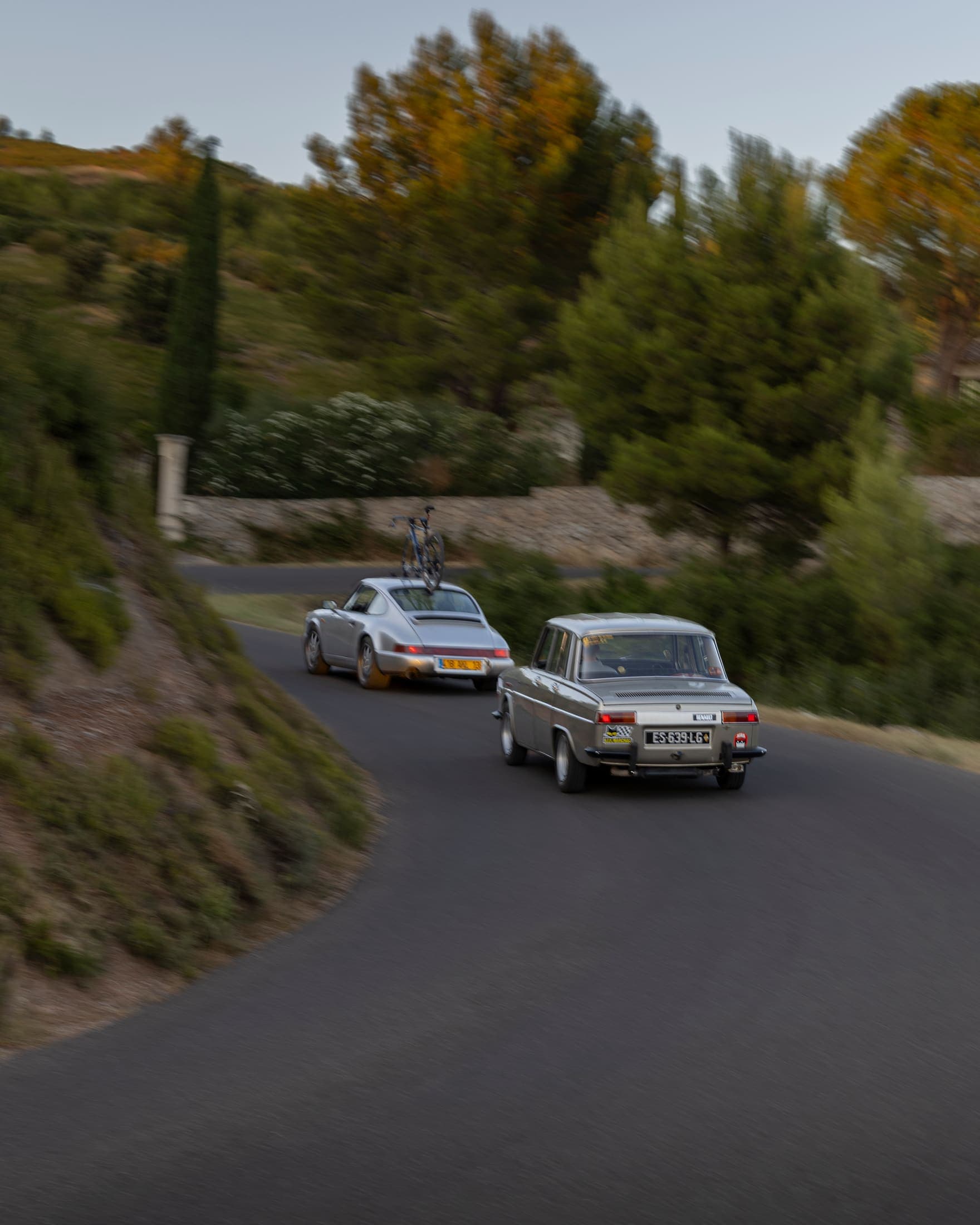 Porsche 911 et Renault 8 Gordini filant sur une route sinueuse