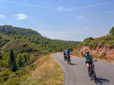 Three cyclists on a winding road through wooded hills with ochre-toned Provence land under a clear blue sky