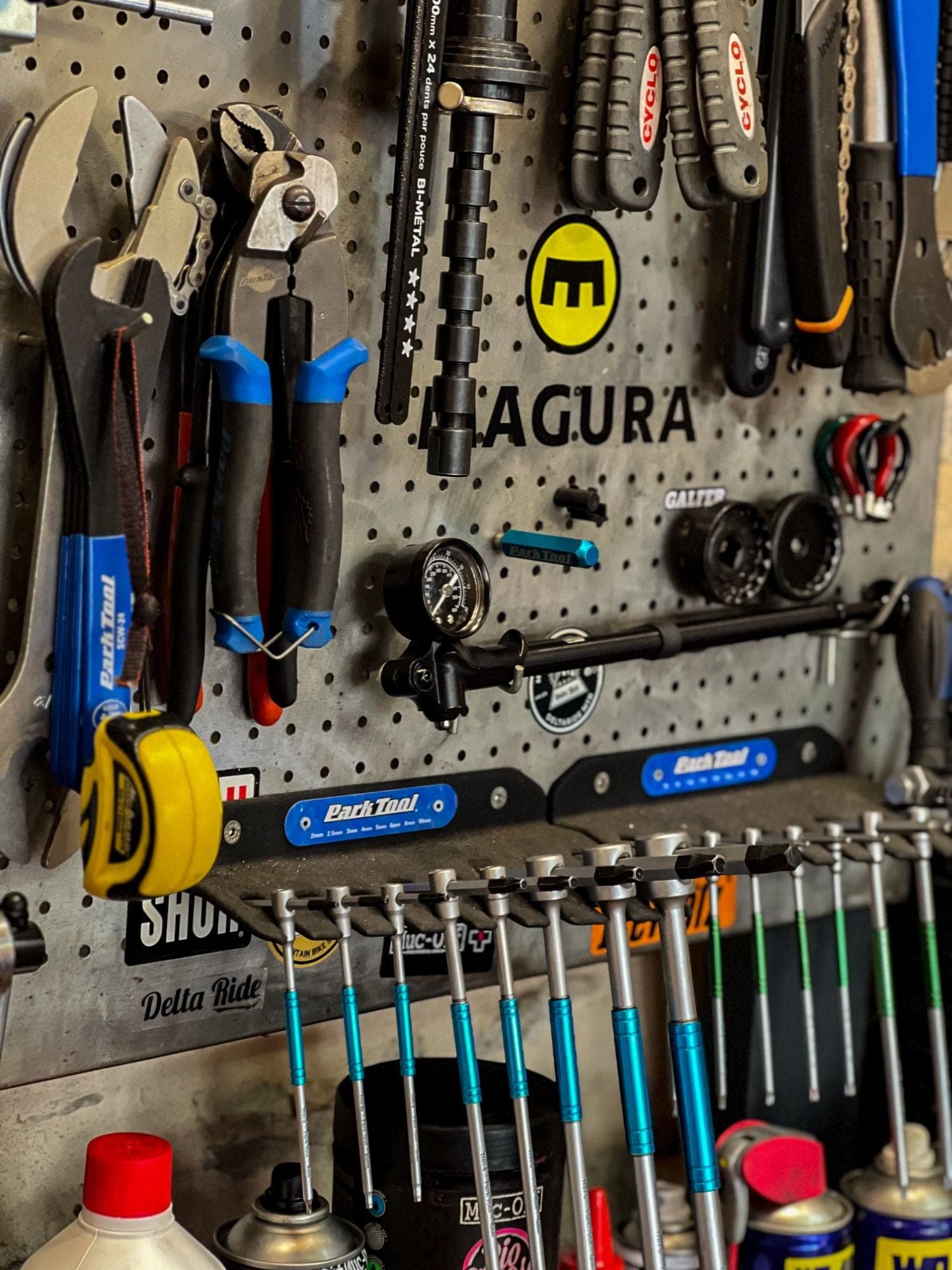 Wall-mounted bike repair tool panel featuring wrenches, pliers and screwdrivers from Park Tool and Agura brands in a bicycle mechanics workshop