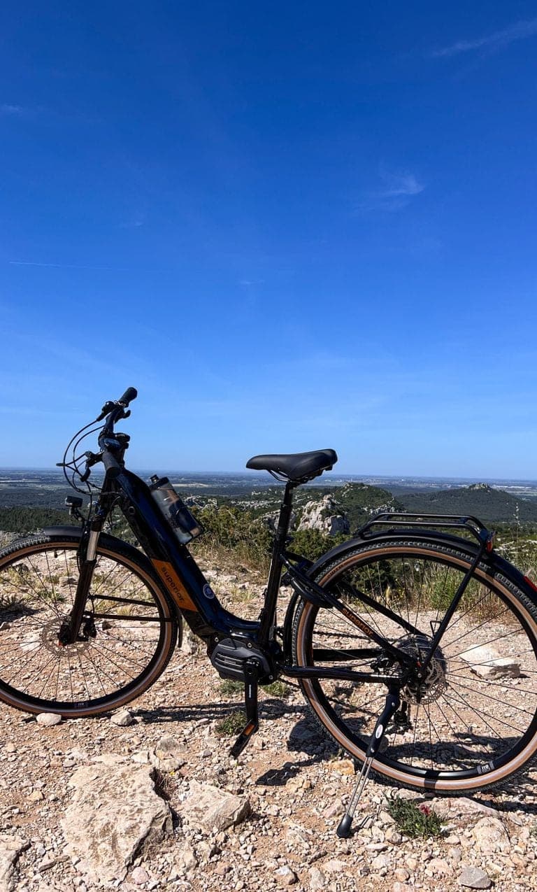 Black electric bike parked on a rocky outcrop with panoramic views of the Provençal countryside and blue sky in the background