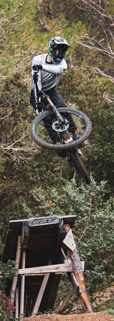 Rider performing an aerial jump on a mountain bike over a wooden ramp in Provence, wearing trial bike helmet and protective gear