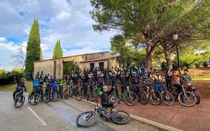 Group of cyclists with bikes and mountain bikes posing in front of a Provençal house under cypress trees during a guided tour in Provence