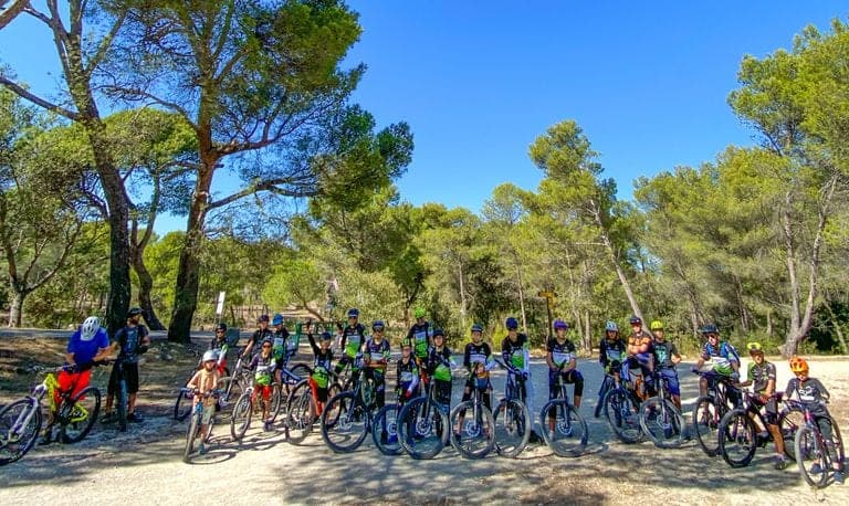Group of cyclists with their bikes lined up on a shaded forest path in Provence on a sunny day